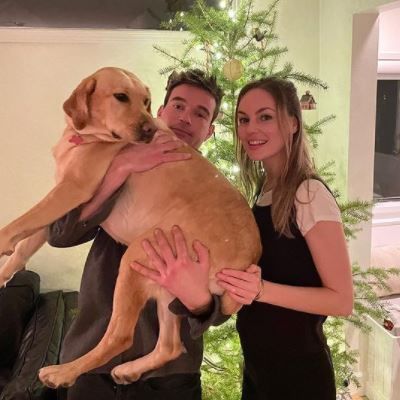 Jesse is carrying the dog as they are posing for the camera. 